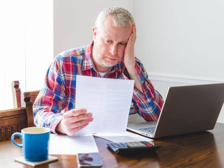 What Happens If You Don’t File Taxes in the USA 9 Overwhelmed man with paperwork and laptop, struggling with financial or personal stress.